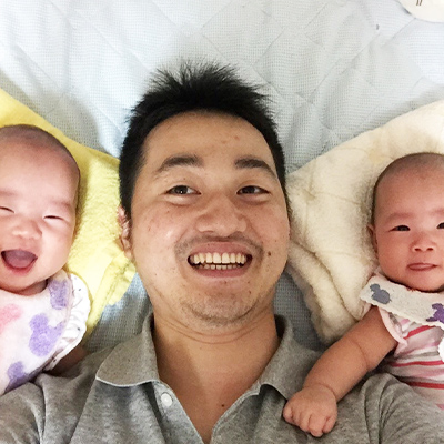 男性社員が双子の赤ちゃんに囲まれている写真