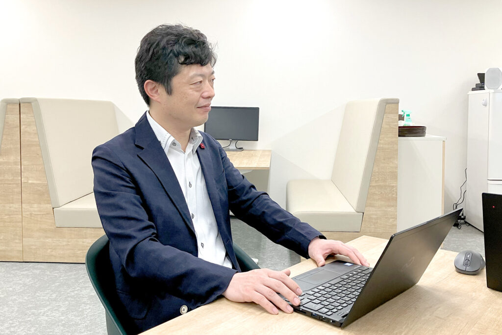 写真:O.T.さんがPCをデスクに置き、少し微笑みながら打合せしている